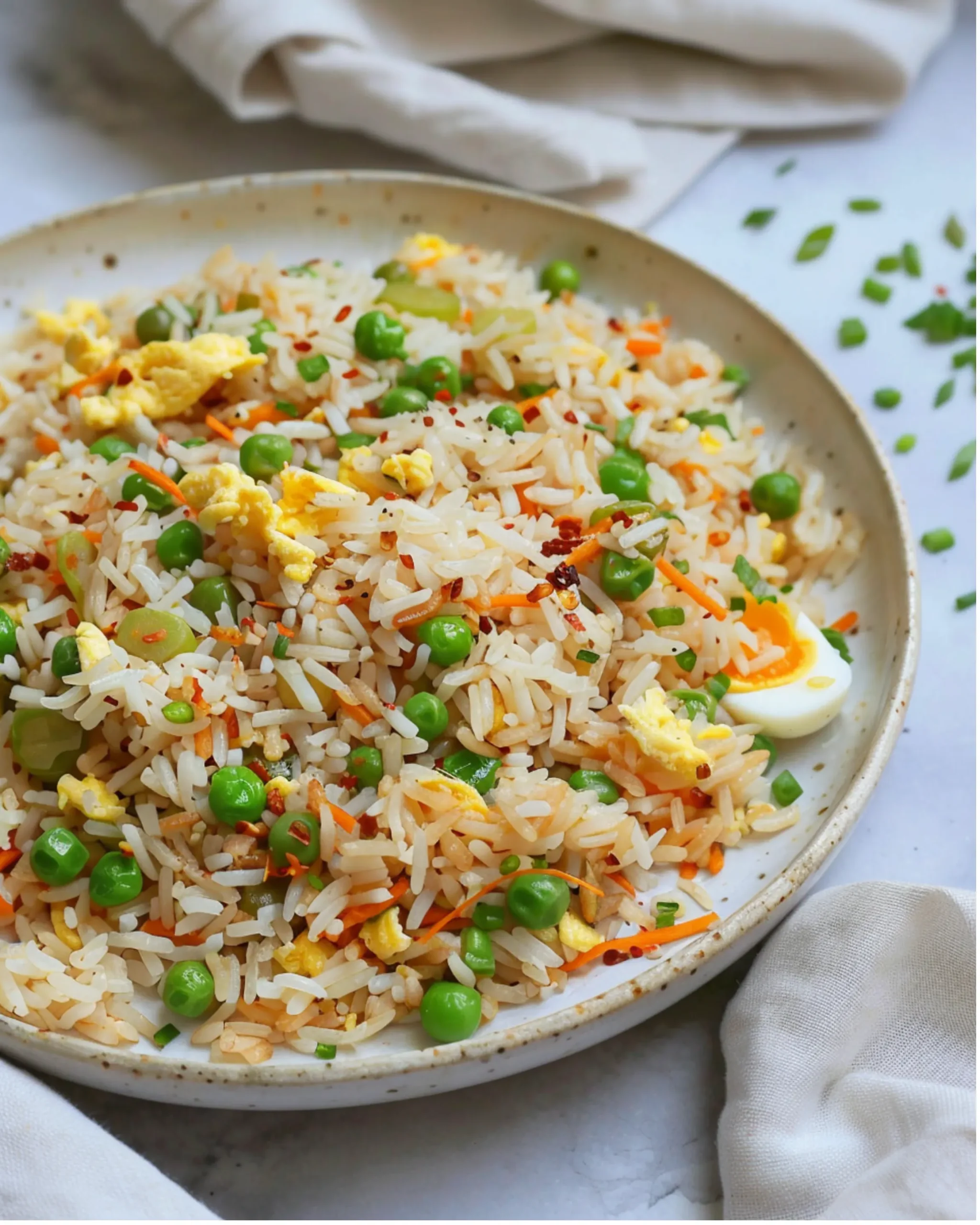 Fried rice served on a white plate with chopped scallions and vegetables