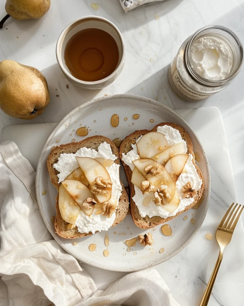 Pear & Honey Ricotta Toast -A Cozy Breakfast Favorite 2 Overhead view of two pear and honey ricotta toasts on parchment paper, topped with fresh pear slices, honey drizzle, and chopped nuts, with a cup of coffee and a linen napkin in natural daylight.