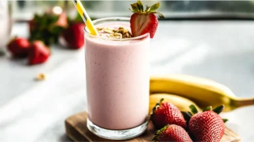 Strawberry banana protein shake topped with fruit in a tall glass.