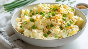 Overhead view of creamy potato salad topped with paprika and green onions in a white bowl