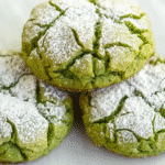 Stack of vibrant green matcha crinkle cookies dusted with powdered sugar on a white ceramic plate