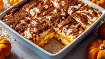 Creamy high protein cottage cheese pumpkin bake in a white baking dish, dusted with cinnamon, with a slice removed to reveal the golden pumpkin filling.