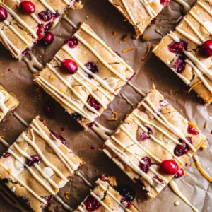 Top-down view of Cranberry White Chocolate Blondies drizzled with melted white chocolate and orange zest.