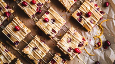 Top-down view of Cranberry White Chocolate Blondies drizzled with melted white chocolate and orange zest.