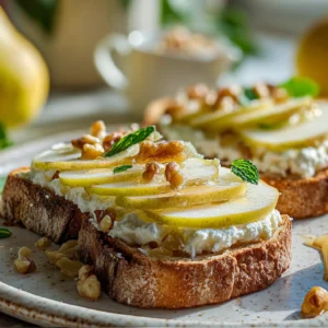Close-up of pear and honey ricotta toast on a rustic white plate, topped with thin pear slices, golden honey drizzle, and crushed walnuts, set on a bright marble countertop with a jar of honey and fresh pears in the background.