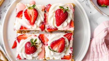 Top-down view of Strawberry Shortcake Cookie Bars topped with frosting and fresh strawberries on a white marble surface.