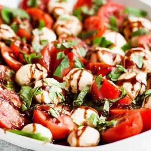Caprese Salad featuredin a white bowl with cherry tomatoes, mozzarella, basil, and balsamic glaze