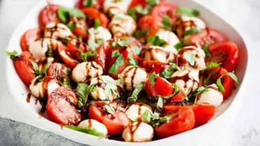 Caprese Salad featuredin a white bowl with cherry tomatoes, mozzarella, basil, and balsamic glaze