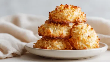 Lemon Coconut Cheesecake Cookies on a white plate with coconut and lemon zest in a modern kitchen setting.