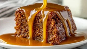 Decadent Sticky Toffee Pudding dripping with golden toffee sauce on white plate